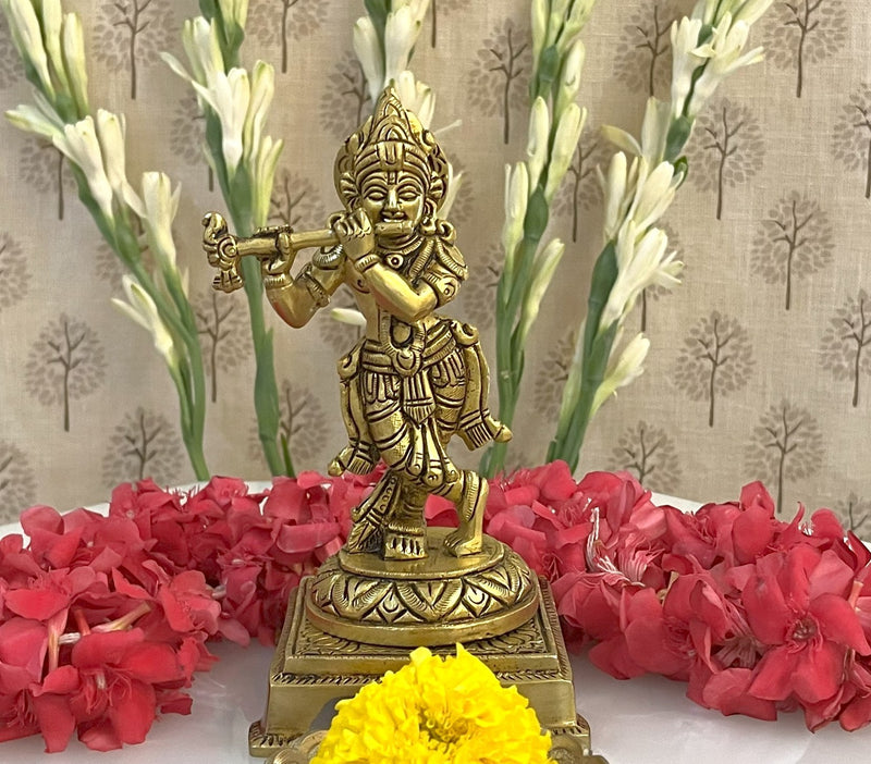 This brass statue of Lord Krishna immersed in playing his flute on a round base is captivatingly beautiful